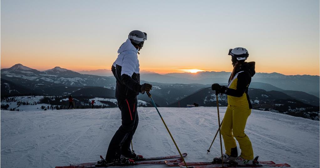 Due persone con gli sci guardano il tramonto